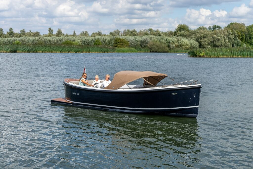 Maxima 750 Flying Lounge sloep met 3 personen op open water, donkerblauwe romp en beige cabrioletkap